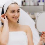 Patient in a clinical setting holding a mirror and smiling at her smooth healthy skin reflecting visible Morpheus8 results after radiofrequency microneedling treatment