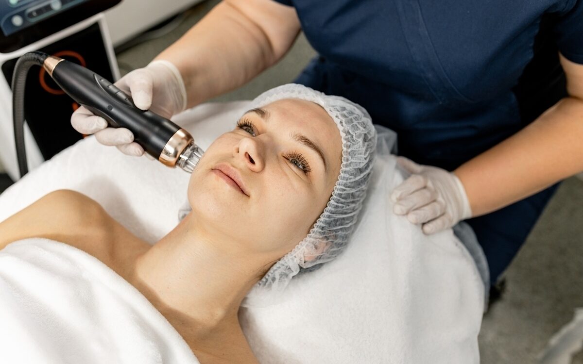 Provider applying a Quantum RF vs Morpheus8 radiofrequency handpiece to a patient's cheek during a non-surgical facial skin tightening treatment session
